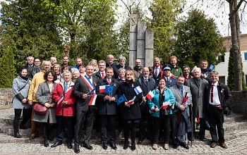 Partnerschaftsgäste vor dem Denkmal in Sztum. Im Vordergrund der Bürgermeister von Sztum und im Hintergrund das Denkmal und viele Bäume.