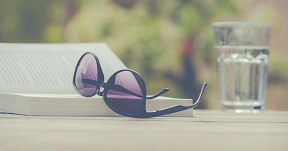 Das Bild zeigt ein aufgeschlagenes Buch im Sonnenlicht, eine Sonnenbrille und ein Glas Wasser.&nbsp;&copy;&nbsp;Pixabay.com