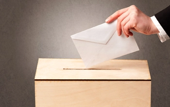 Zuerkennen ist eine menschliche Hand, die einen Briefumschlag in eine Wahlurne legt.